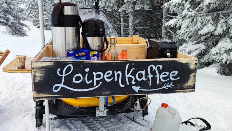 Mobiler Kaffeestand im Schnee mit der Aufschrift 'Loipenkaffee'.