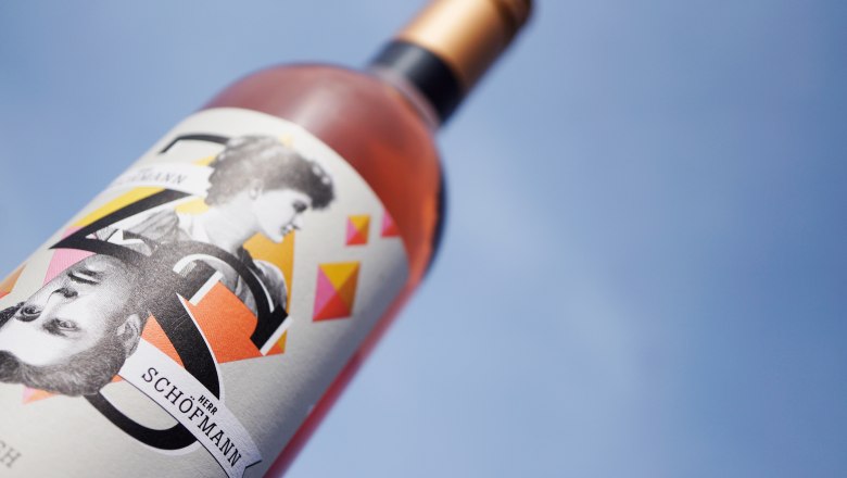 Nahaufnahme einer Weinflasche mit k&uuml;nstlerischem Etikett vor blauem Himmel.