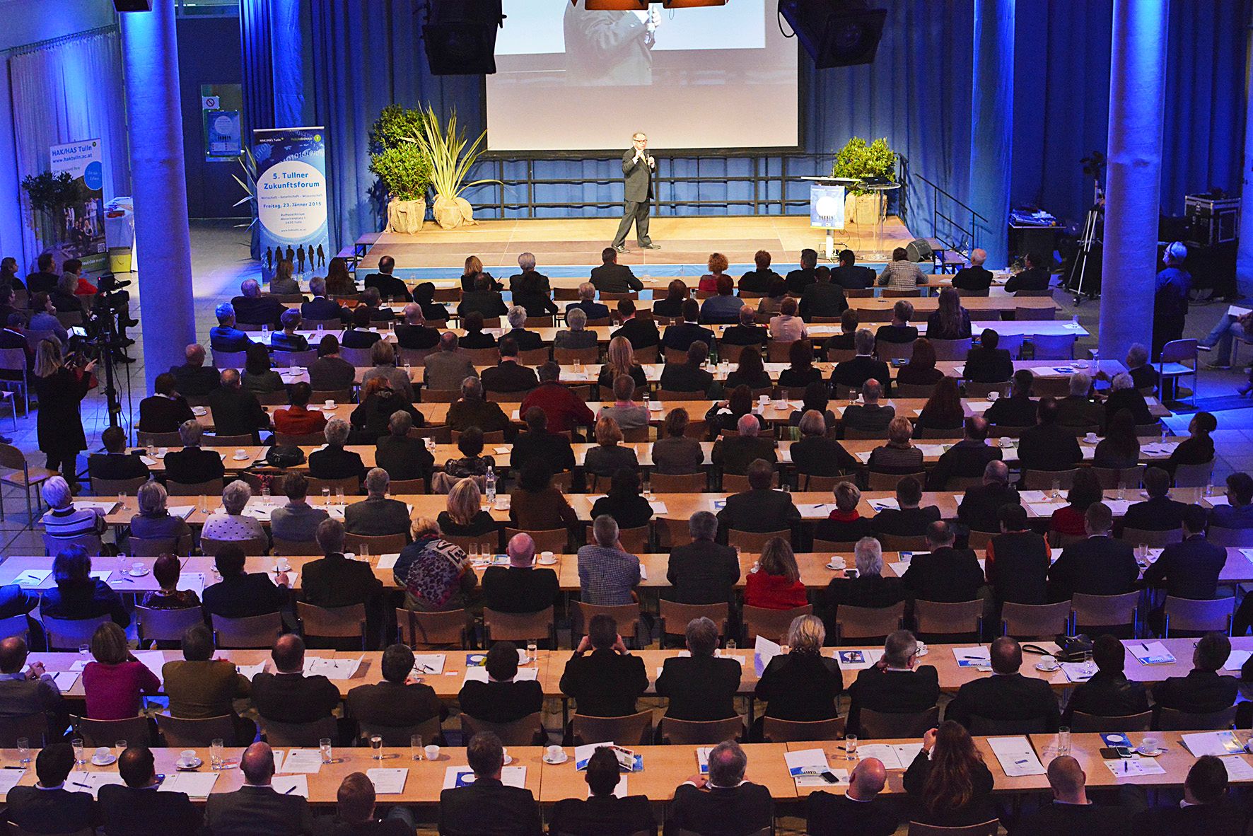 Ein Redner spricht vor einem großen Publikum in einem Konferenzsaal.
