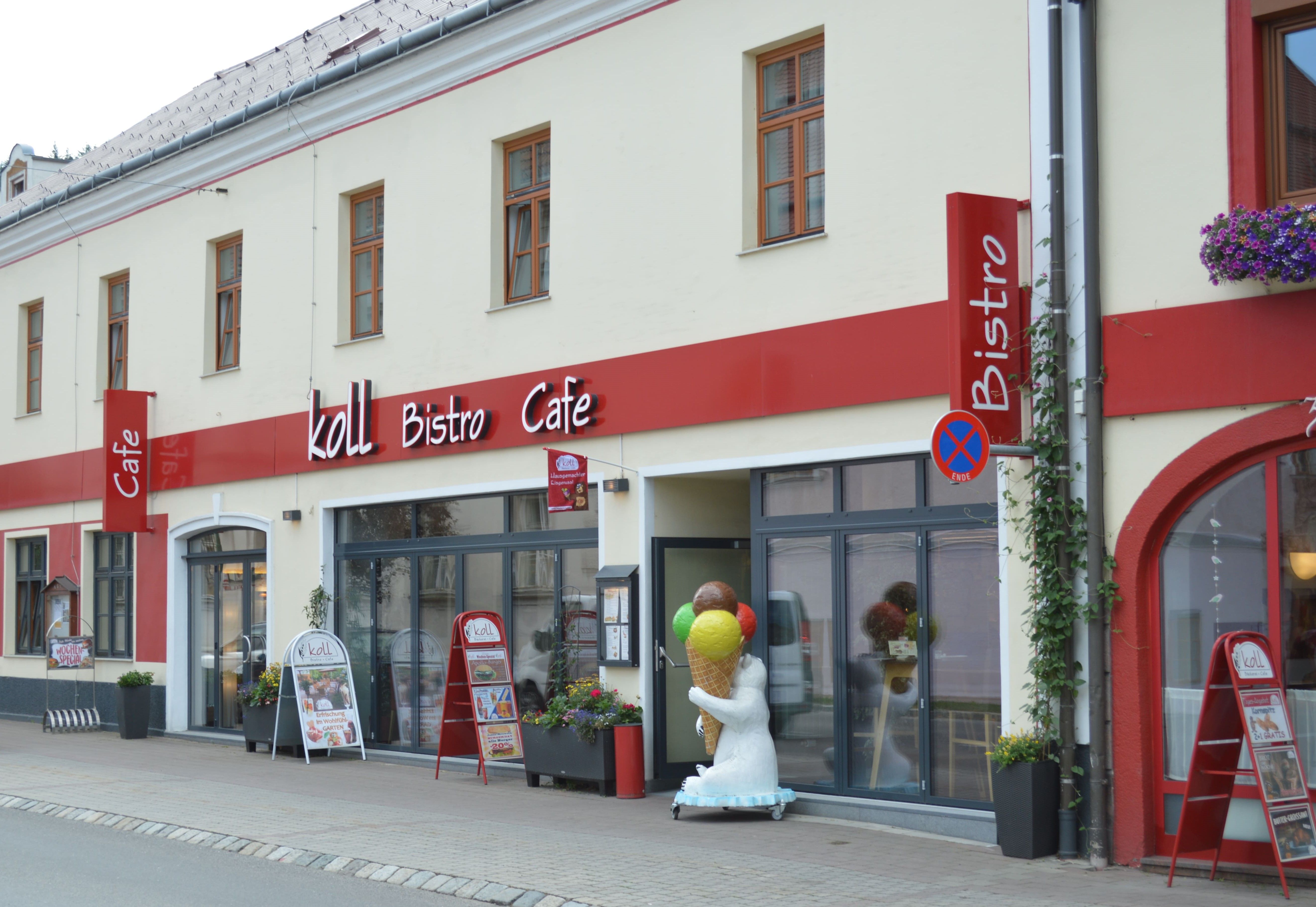Außenansicht des Koll Bistro Cafés mit rotem Schild und Eisbärfigur mit Eis-Stanizel vor dem Eingang.