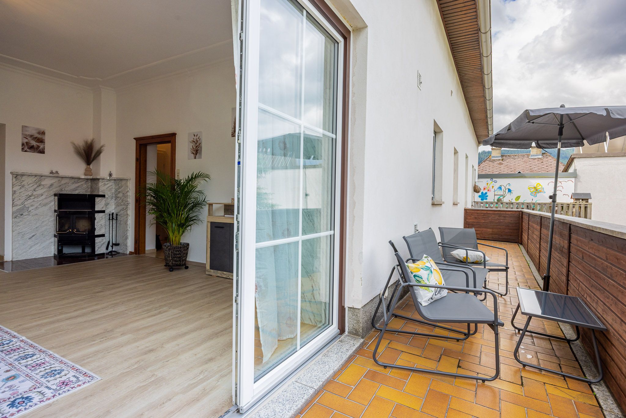 Blick von einer Terrasse in ein Wohnzimmer mit Kamin und Pflanzen.