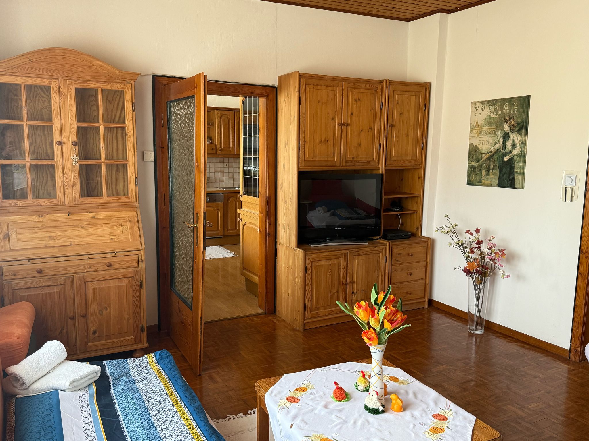 Wohnzimmer mit Holzmöbeln, einem Tisch mit Blumen und einem Fernseher.