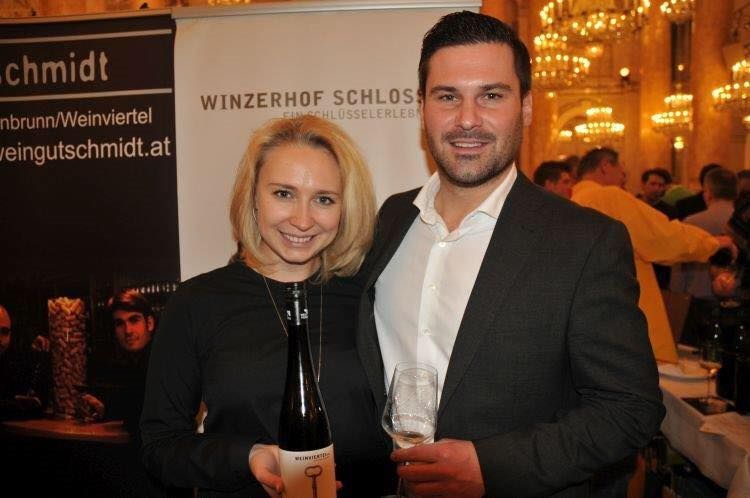 Ein Paar hält eine Weinflasche und ein Weinglas vor einem Banner mit der Aufschrift 'Winzerhof Schlosser'.