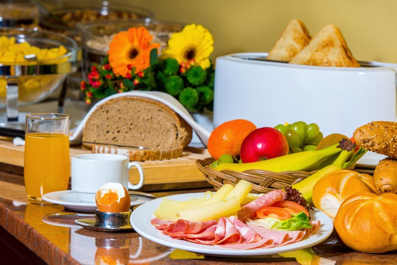 Frühstücksbuffet mit Brot, Aufschnitt, Käse, Obst, Brötchen, Saft und Ei.