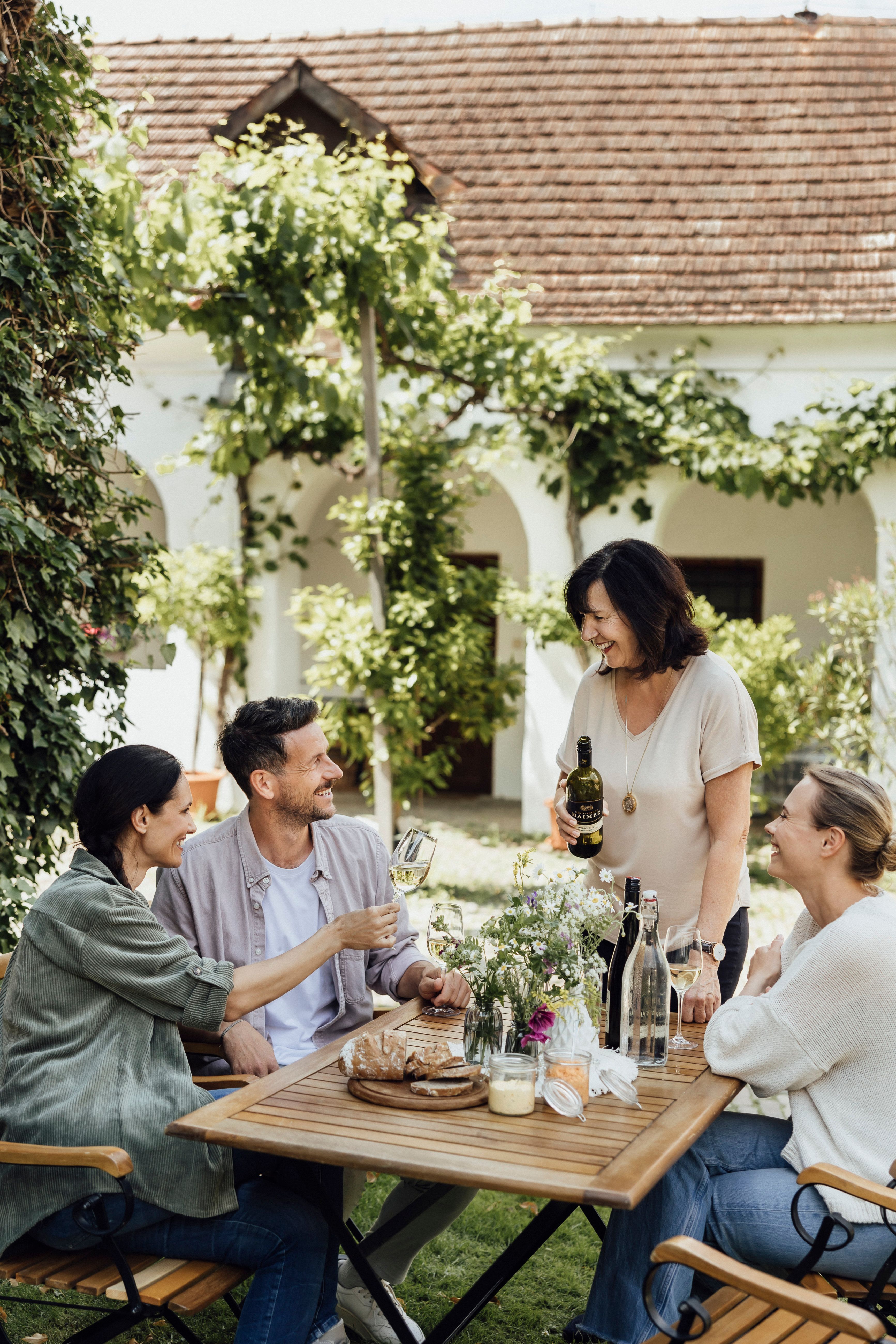 Vier Personen sitzen an einem Tisch im Freien und genießen Wein und Brot.