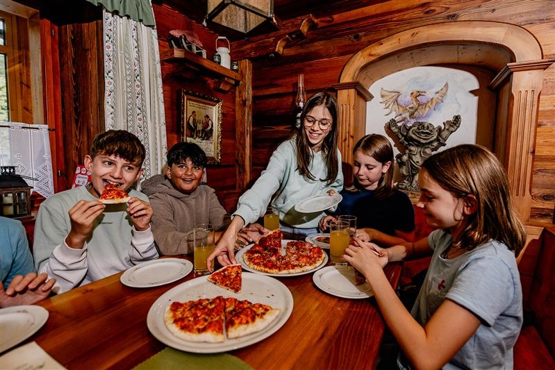 Kinder essen Pizza in einem rustikalen Raum mit Holzwänden.