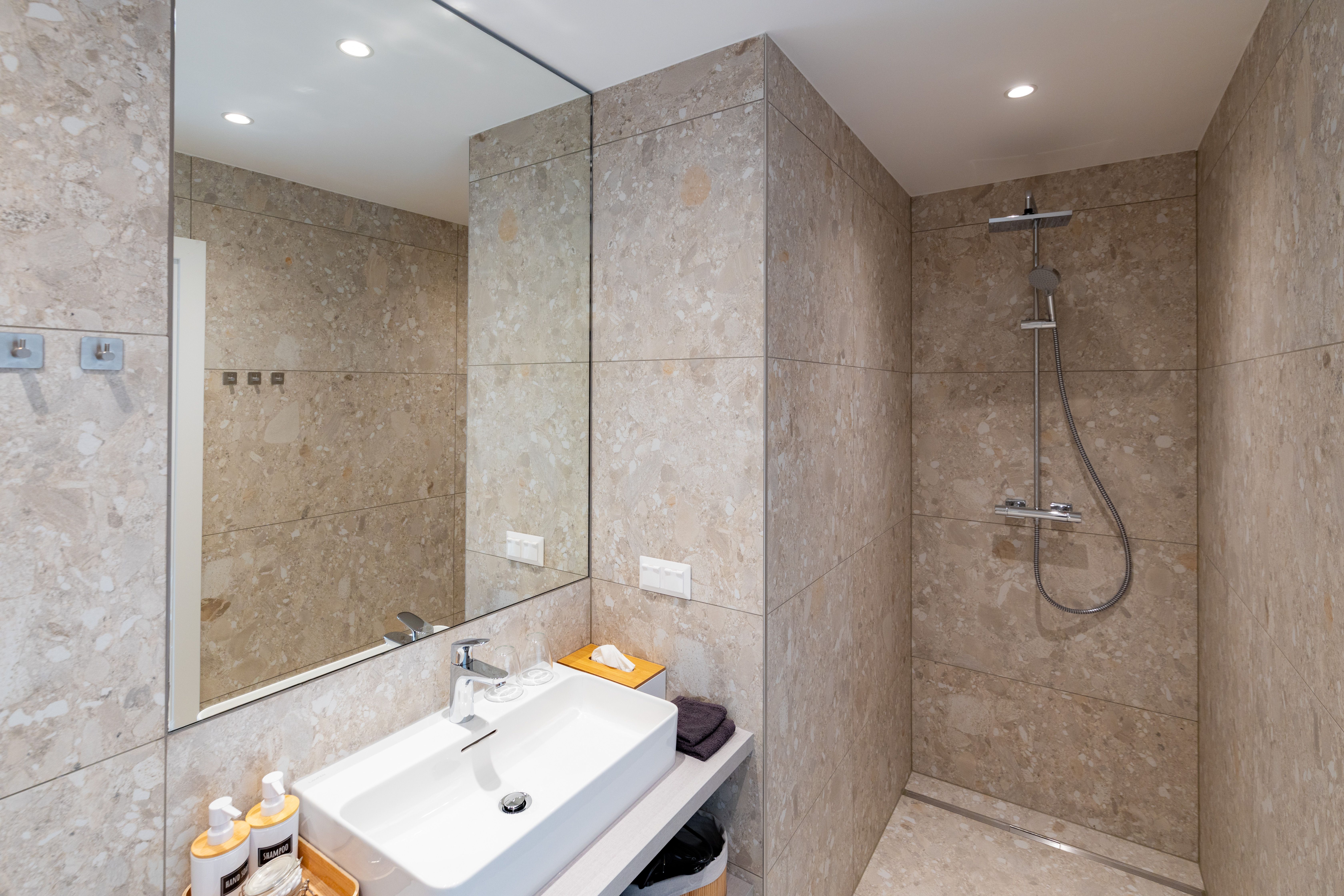 Modernes Badezimmer mit beiger Fliesenwand, Waschbecken, Spiegel und Regendusche.