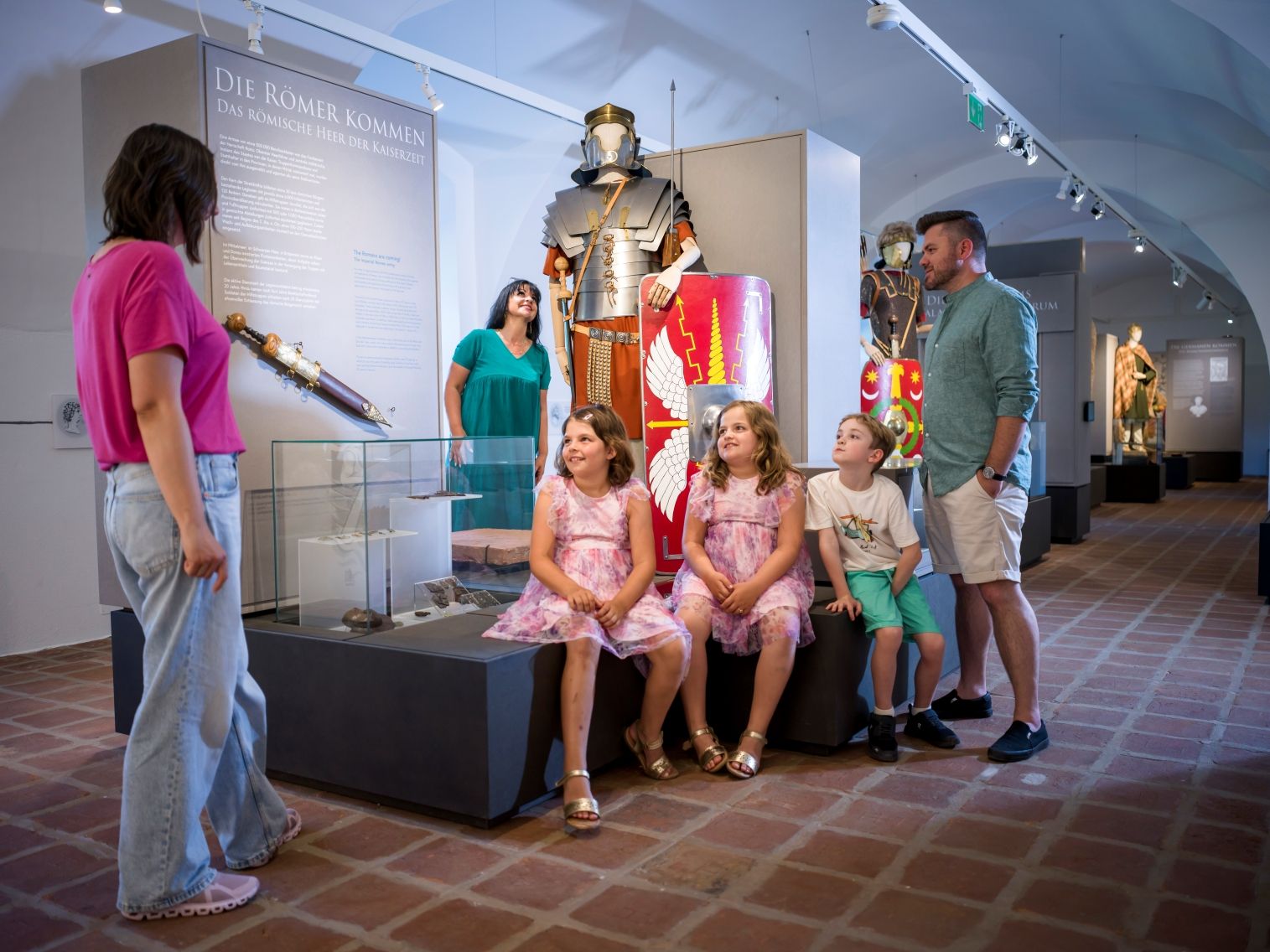 Kinder sitzen vor römischen Rüstung im Stadtmuseum, Erwachsene stehen daneben