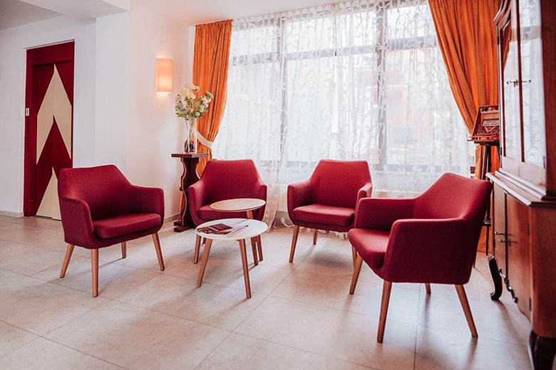 Gemütliche Sitzecke mit roten Sesseln und kleinem Tisch vor einem Fenster mit Vorhängen.