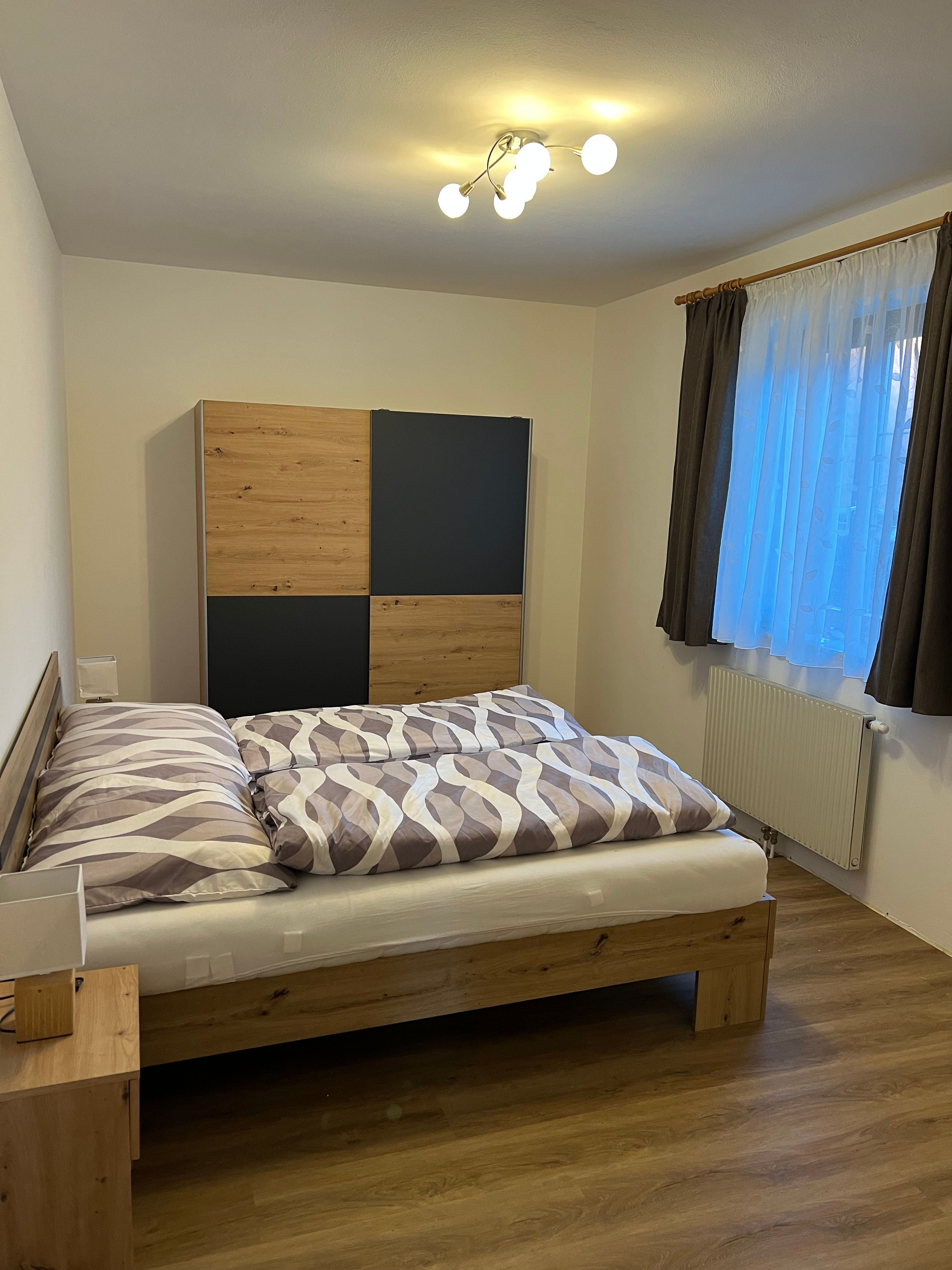 Ein gemütliches Doppelzimmer mit einem Holzbett, einem Kleiderschrank und einem Fenster mit Vorhängen.