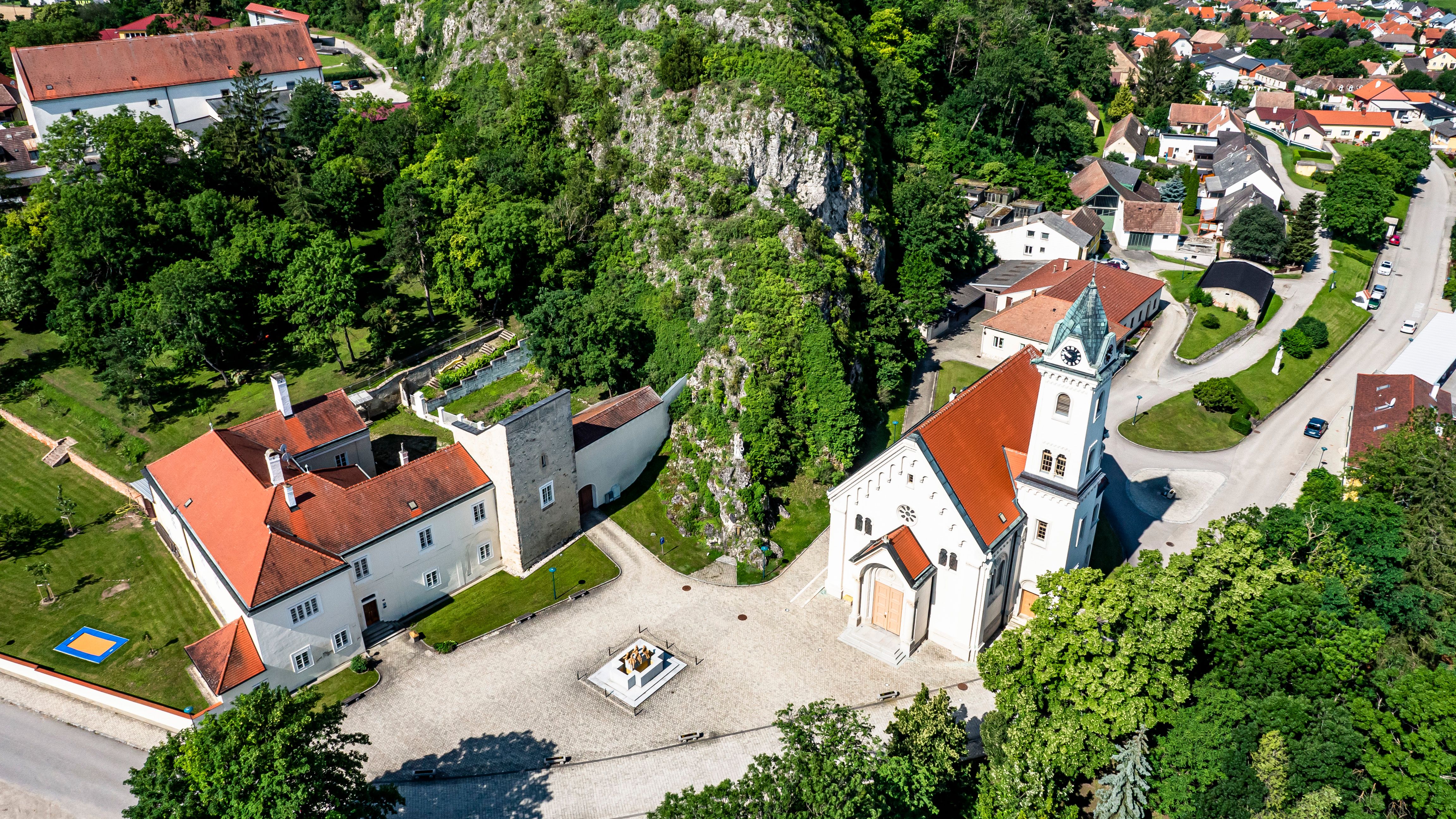 Luftaufnahme der Pfarrkirche Staatz mit umliegenden Gebäuden und Grünflächen.