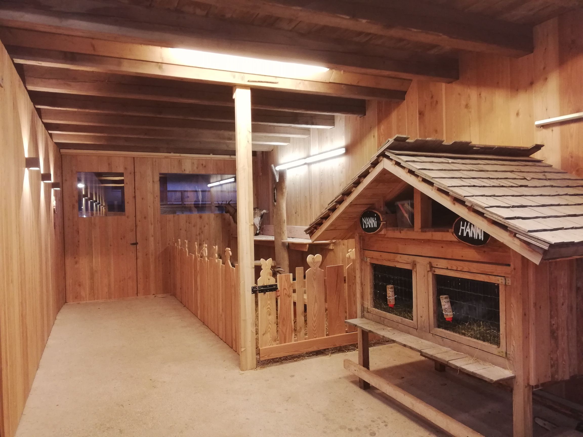 Innenansicht eines Ziegenstalls aus Holz mit Ziegengehege und kleinem Häuschen.