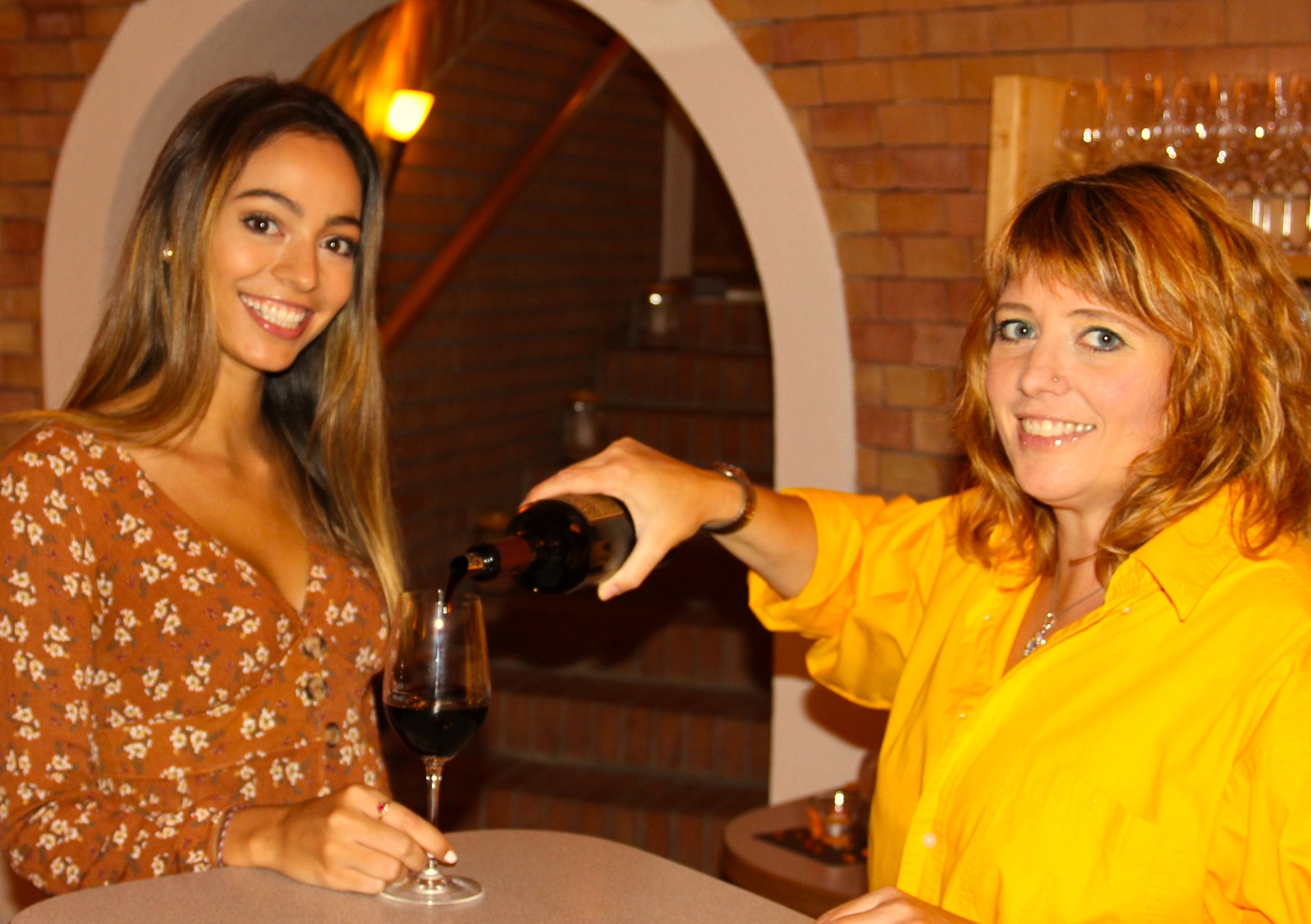 Zwei Frauen in einem Weinkeller, eine schenkt der anderen Wein ein.