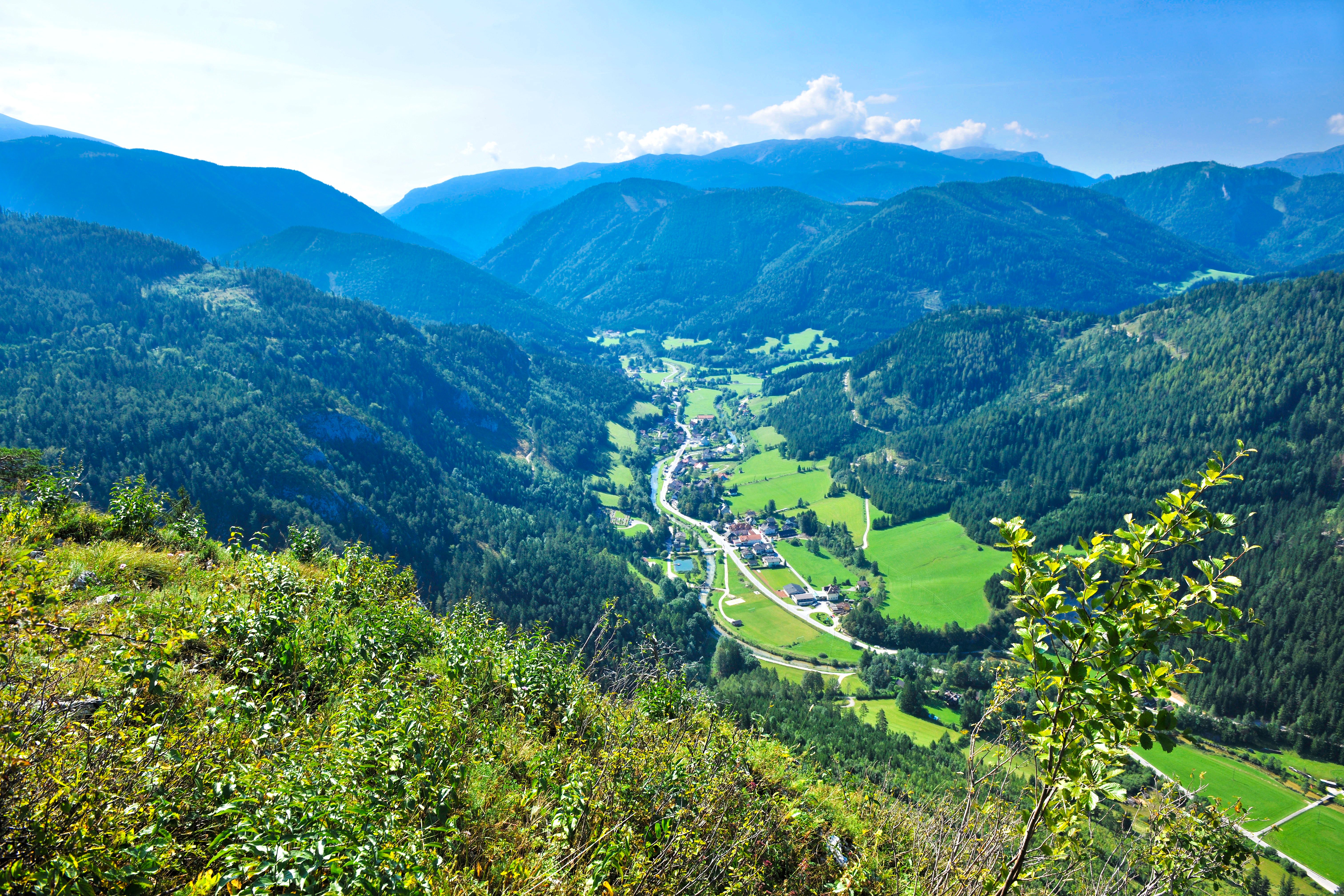 Panoramablick auf ein grünes Tal mit Bergen im Hintergrund.
