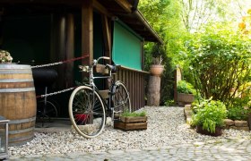 Rustikaler Eingangsbereich mit Fahrrad, Holzfass und Pflanzen.