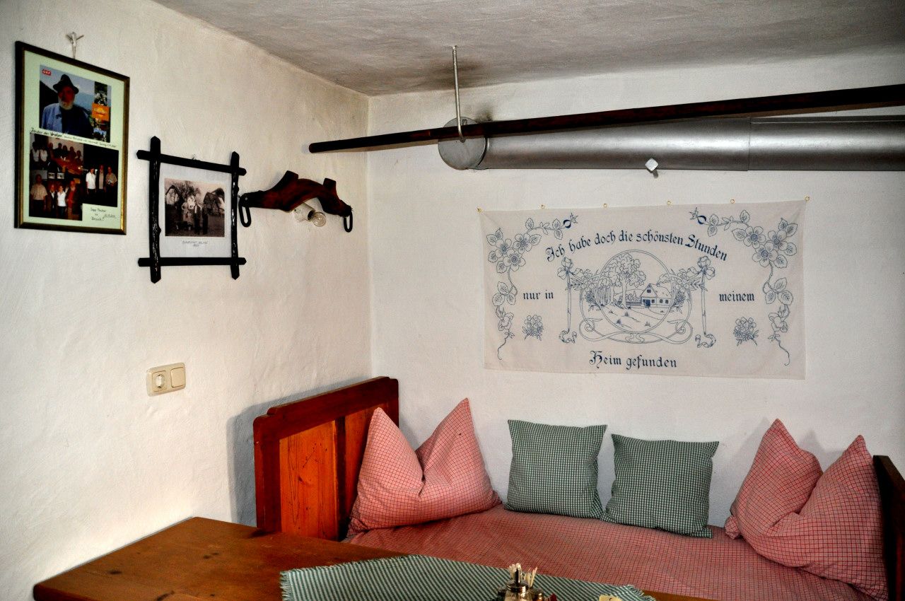 Innenansicht eines traditionellen Zimmers mit Holzmöbeln, Kissen und Wanddekorationen im Bauernhausmuseum Ablass.