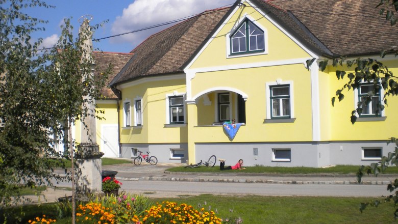 Gelbes G&auml;stehaus mit Blumenbeet und Fahrr&auml;dern davor.