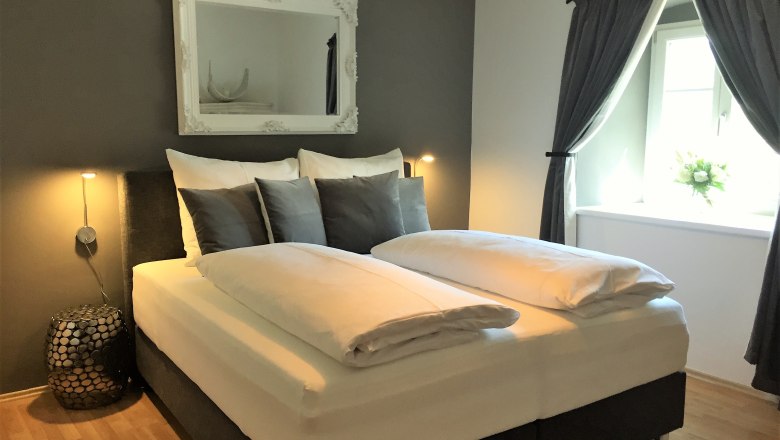 Modernes Schlafzimmer mit Doppelbett, grauen Wänden und dekorativem Spiegel.