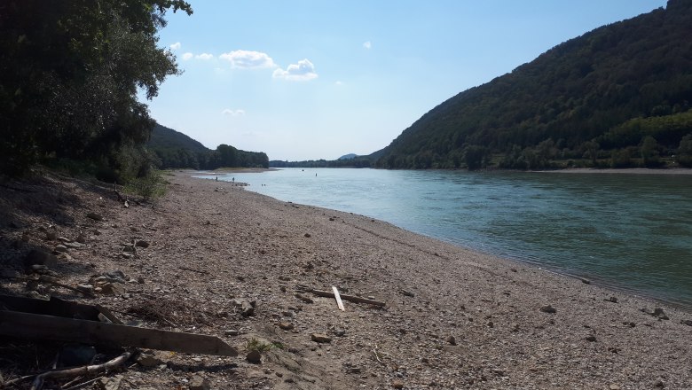 Kiesstrand an der Donau mit bewaldeten Hügeln im Hintergrund.