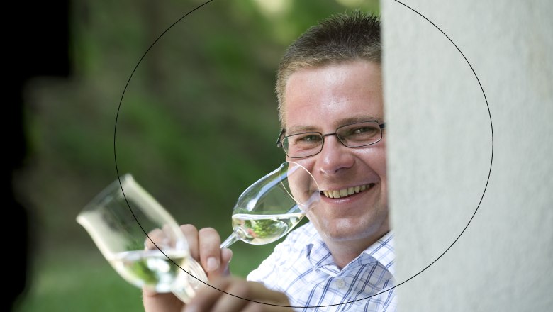 Mann mit Brille h&auml;lt zwei Weingl&auml;ser und l&auml;chelt.