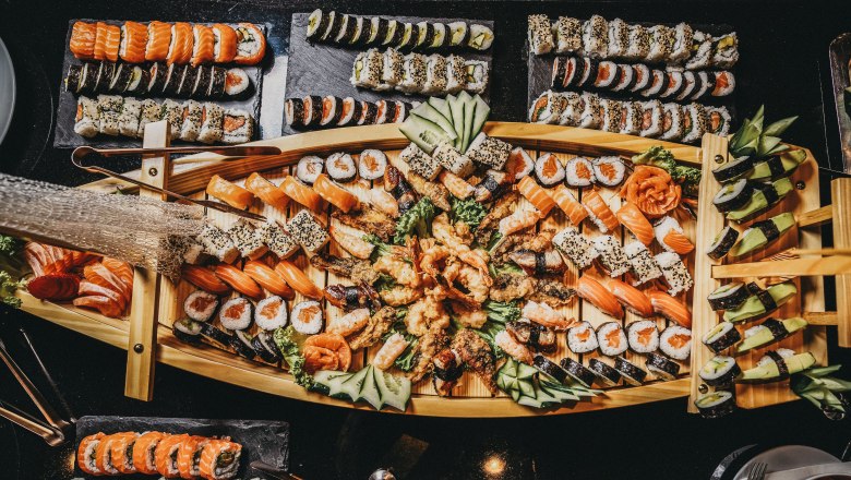 Ein reichhaltiges Sushi-Buffet auf einem Holztablett, dekoriert mit verschiedenen Sushi- und Sashimi-Sorten, Gurken und Ingwer.