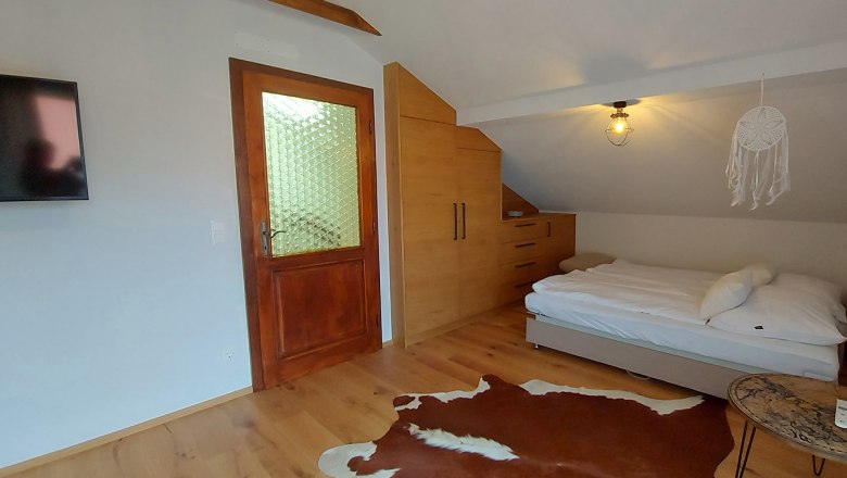 Schlafzimmer mit Holzboden, Bett, Schrank, T&uuml;r und Fernseher.