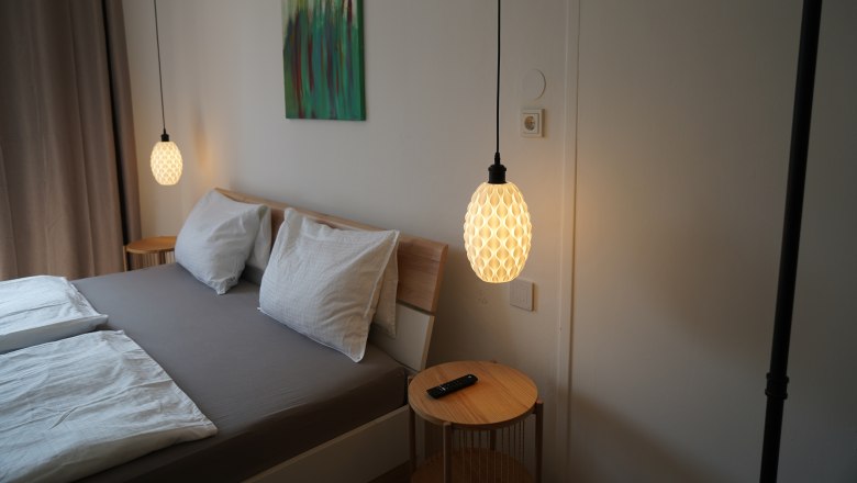 Ein modernes Schlafzimmer mit Doppelbett, zwei hängenden Lampen und einem kleinen Tisch mit Fernbedienung.