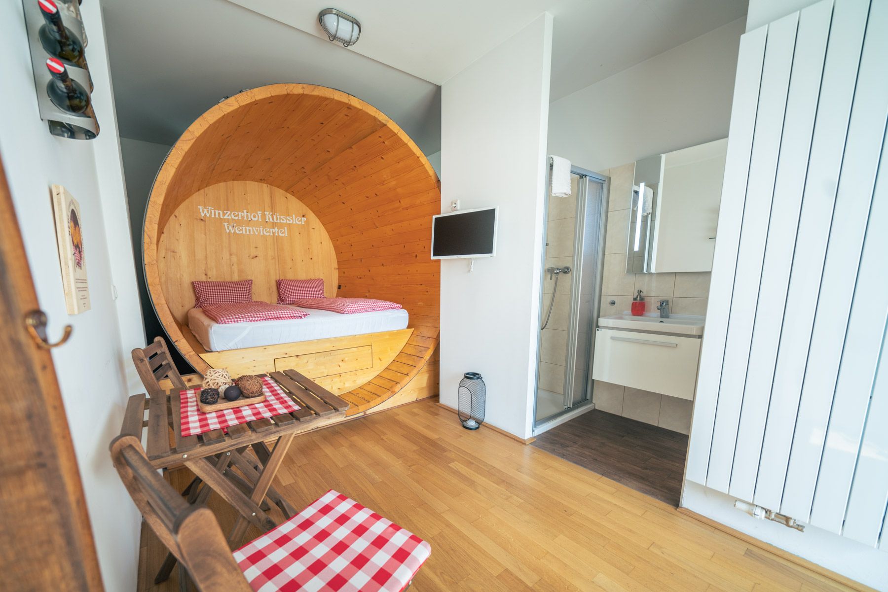 Innenansicht einer Suite mit Bett in einem großen Weinfass, kleinem Tisch mit Stühlen und Badezimmer.