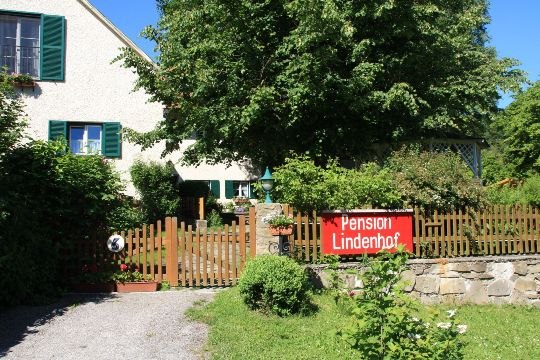 Ein Haus mit Garten und einem Schild "Pension Lindenhof" am Holzzaun.