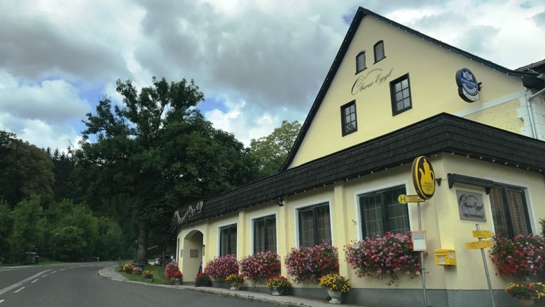 Gasthof Oberer Eggl mit Blumen und Bushaltestelle.