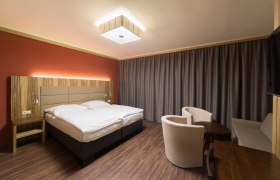 Modern eingerichtetes Hotelzimmer mit Doppelbett, Holzmöbeln und Vorhängen.