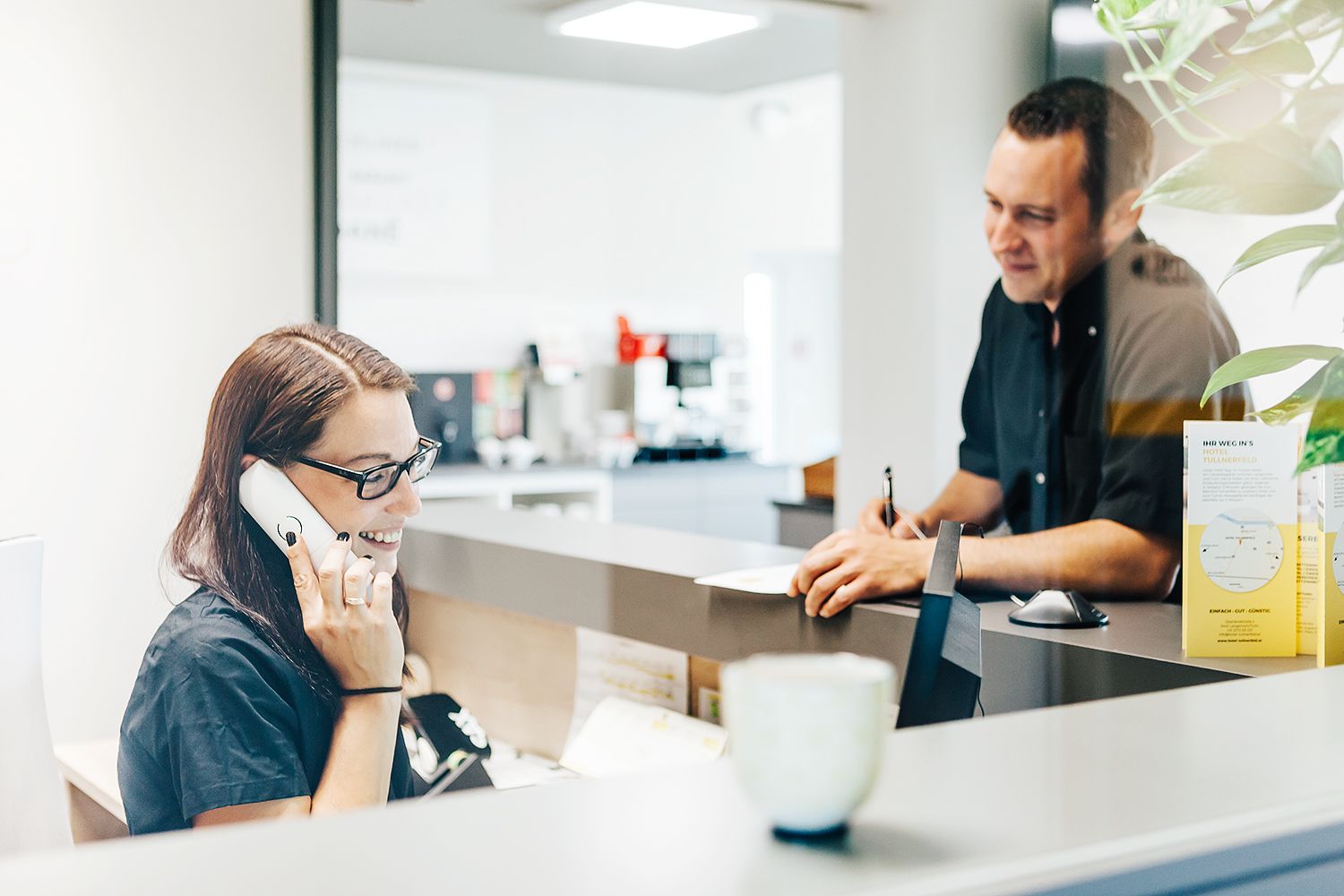 Rezeptionistin, welche telefoniert, mit einem Gast an der Rezeption.