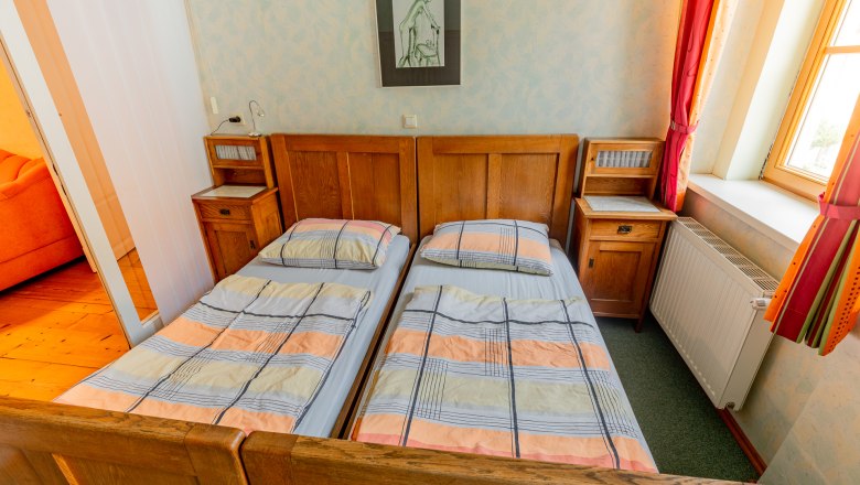 Ein Schlafzimmer mit zwei Einzelbetten, Holzmöbeln und einem Fenster mit roten Vorhängen.