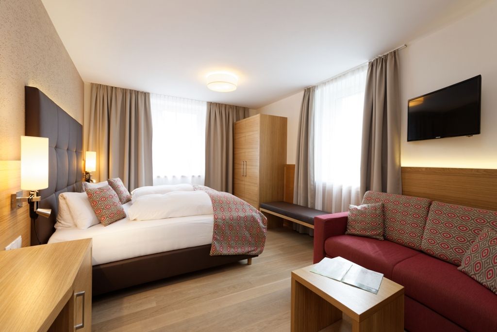 Modernes Hotelzimmer mit Doppelbett, Sofa, Schrank und Fernseher.