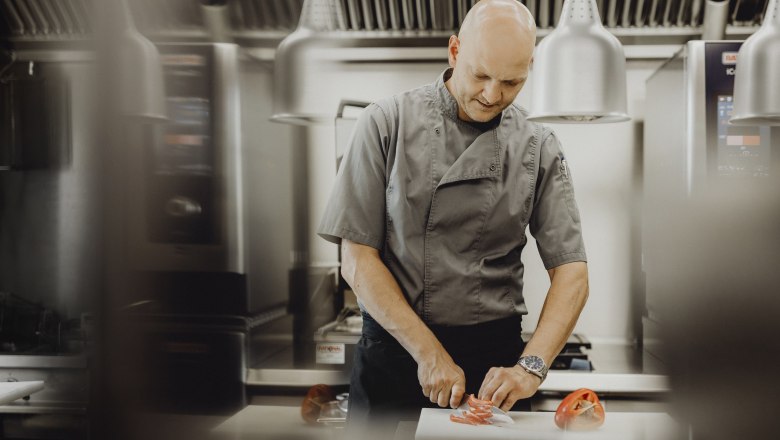 Ein Koch in grauer Uniform schneidet Paprika in einer modernen Küche.