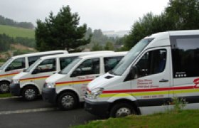 Vier wei&szlig;e Transporter mit gelben und roten Streifen parken nebeneinander auf einem Parkplatz.
