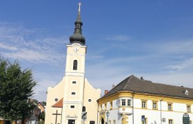 Pfarrkirche mit Turm und angrenzendem Pfarrhof bei klarem Himmel.