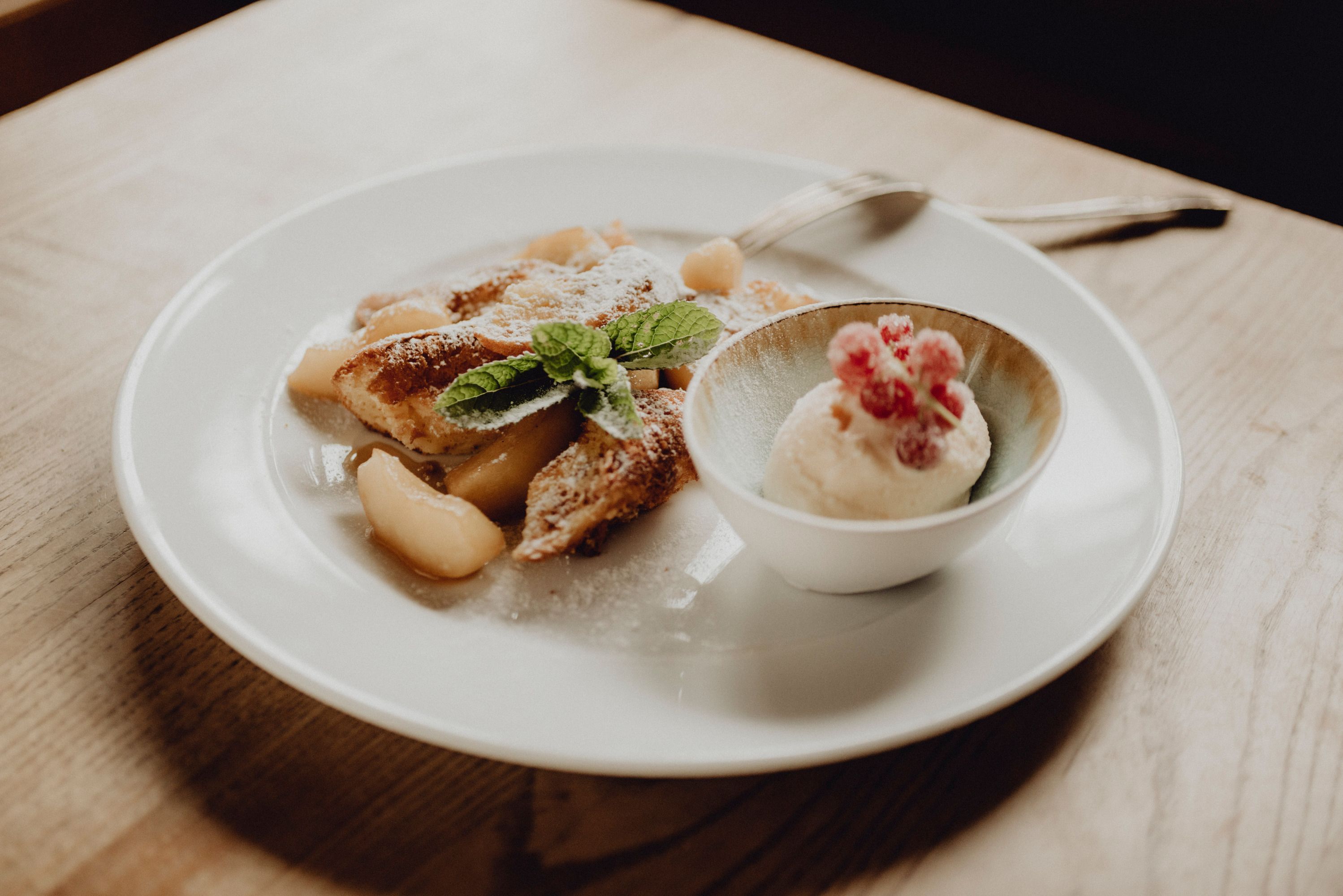 Ein Teller mit Apfelschmarren und einer Schale Topfen-Rum-Eis, garniert mit Minzblättern und roten Beeren.
