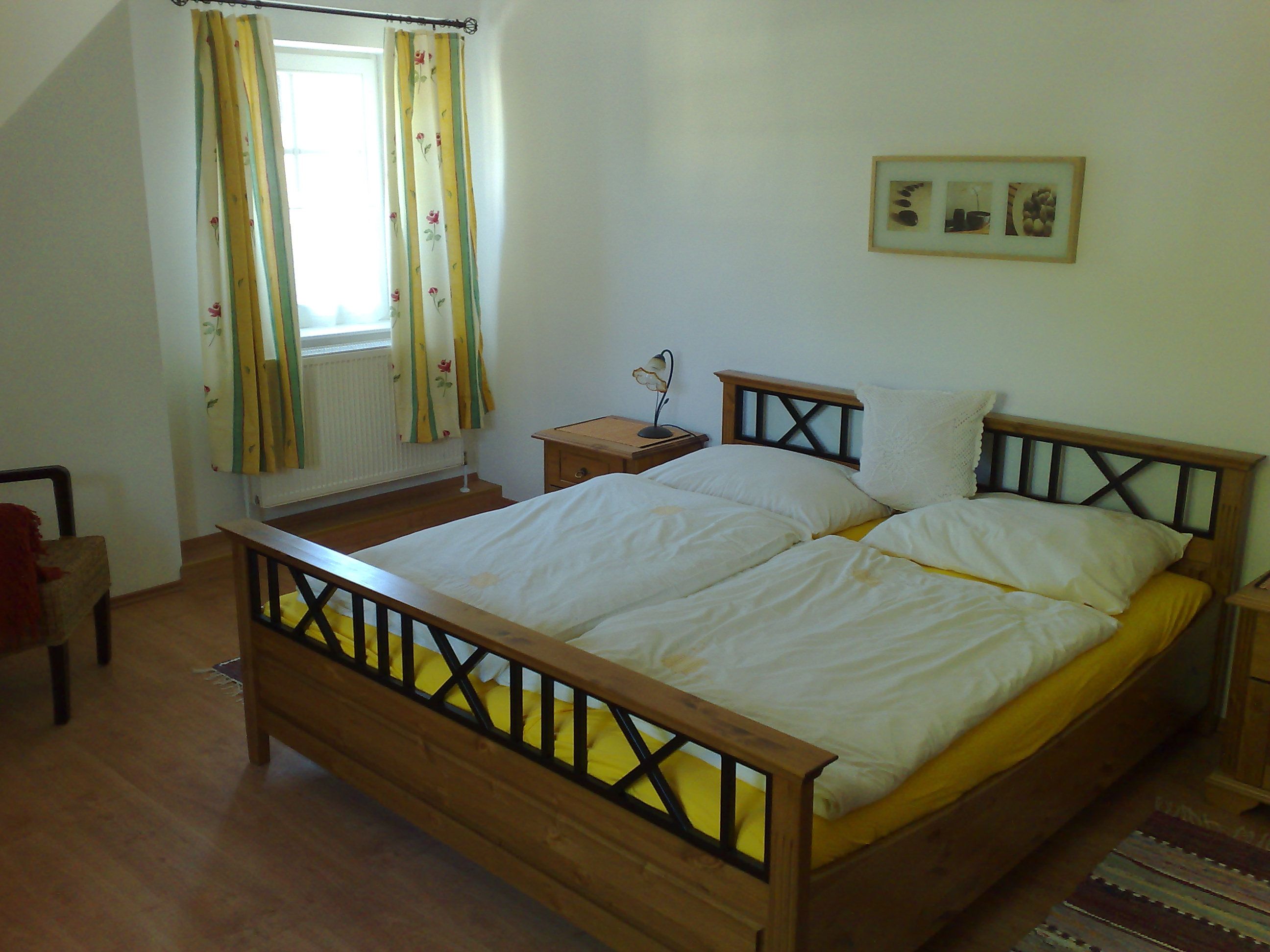 Schlafzimmer mit Doppelbett, gelber Bettwäsche, Holzmöbeln und Blumenvorhängen.