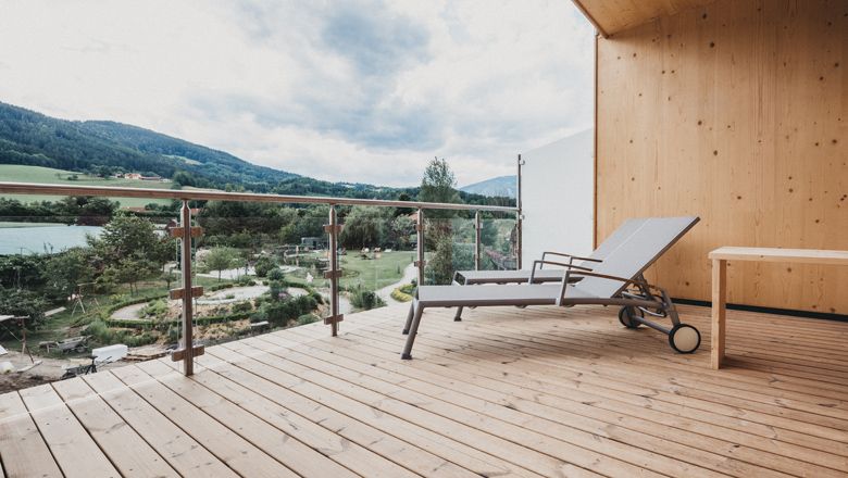 Holzterrasse mit Liegestuhl und Blick auf grüne Landschaft und Berge.