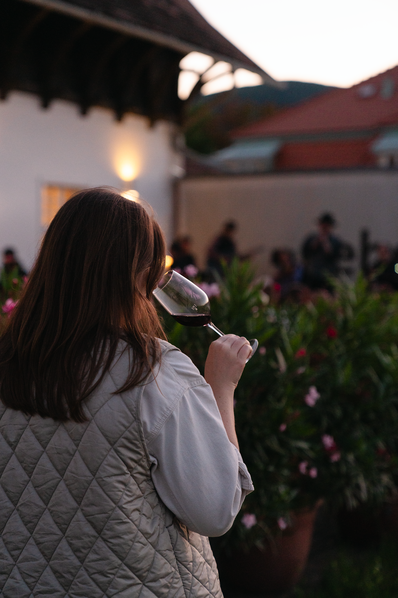 In der sanften Abenddämmerung genießt eine Person ein Glas Wein, während die blühenden Pflanzen um sie herum eine einladende Atmosphäre schaffen. Die harmonische Verbindung von Natur und Kulinarik lädt dazu ein, die regionalen Köstlichkeiten zu entdecken und die Seele baumeln zu lassen.