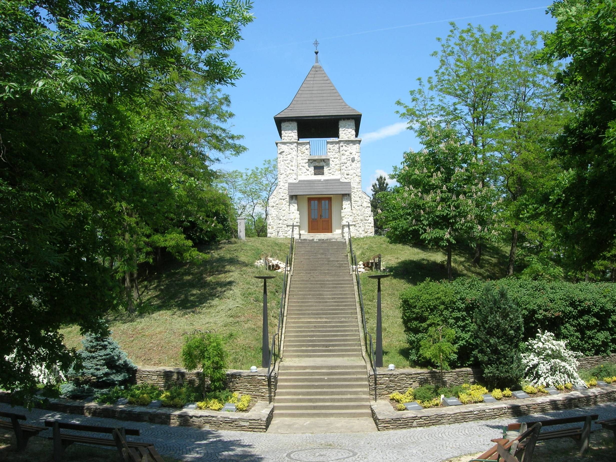 Steinturm auf einem Hügel mit Treppe und grüner Umgebung.