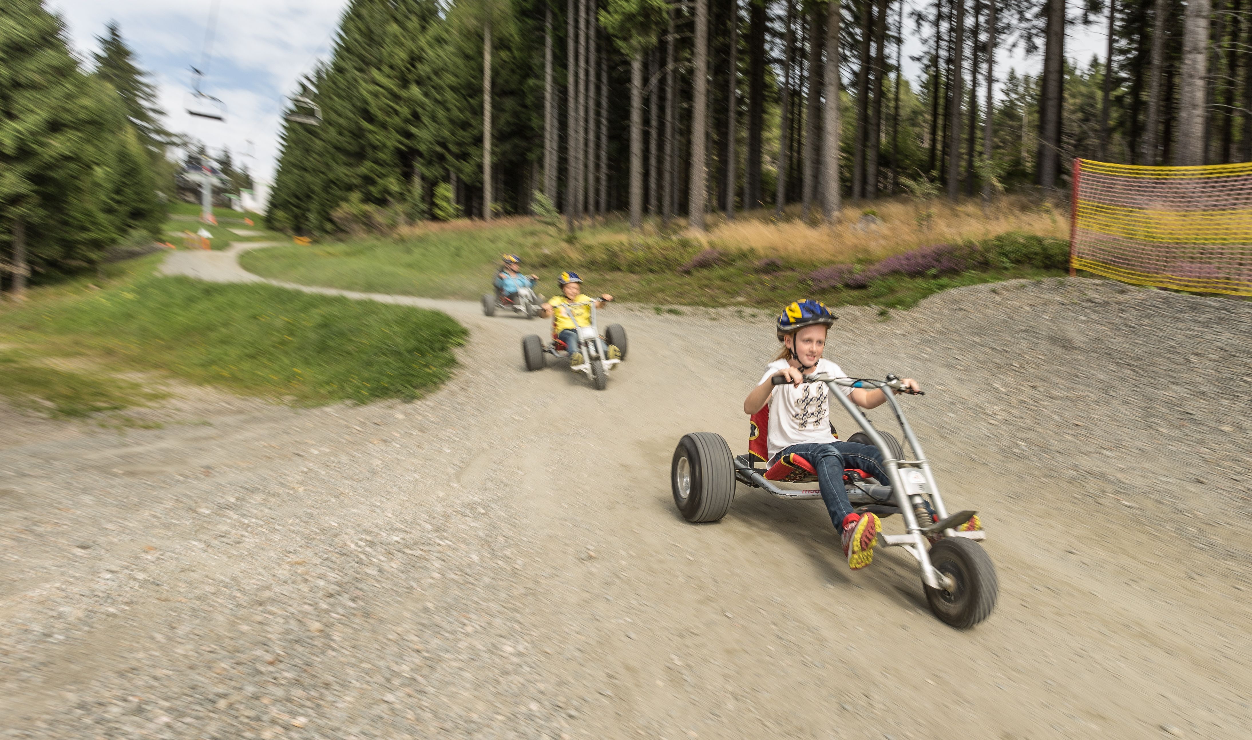 Kinder fahren auf Mountaincarts einen Weg entlang.
