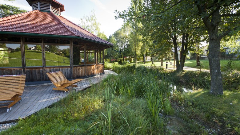 Holzpavillon mit Liegestühlen in einem grünen Park.