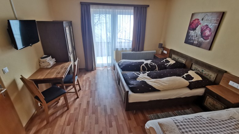 Gem&uuml;tliches Schlafzimmer mit Doppelbett, Tisch, St&uuml;hlen und Balkonzugang.