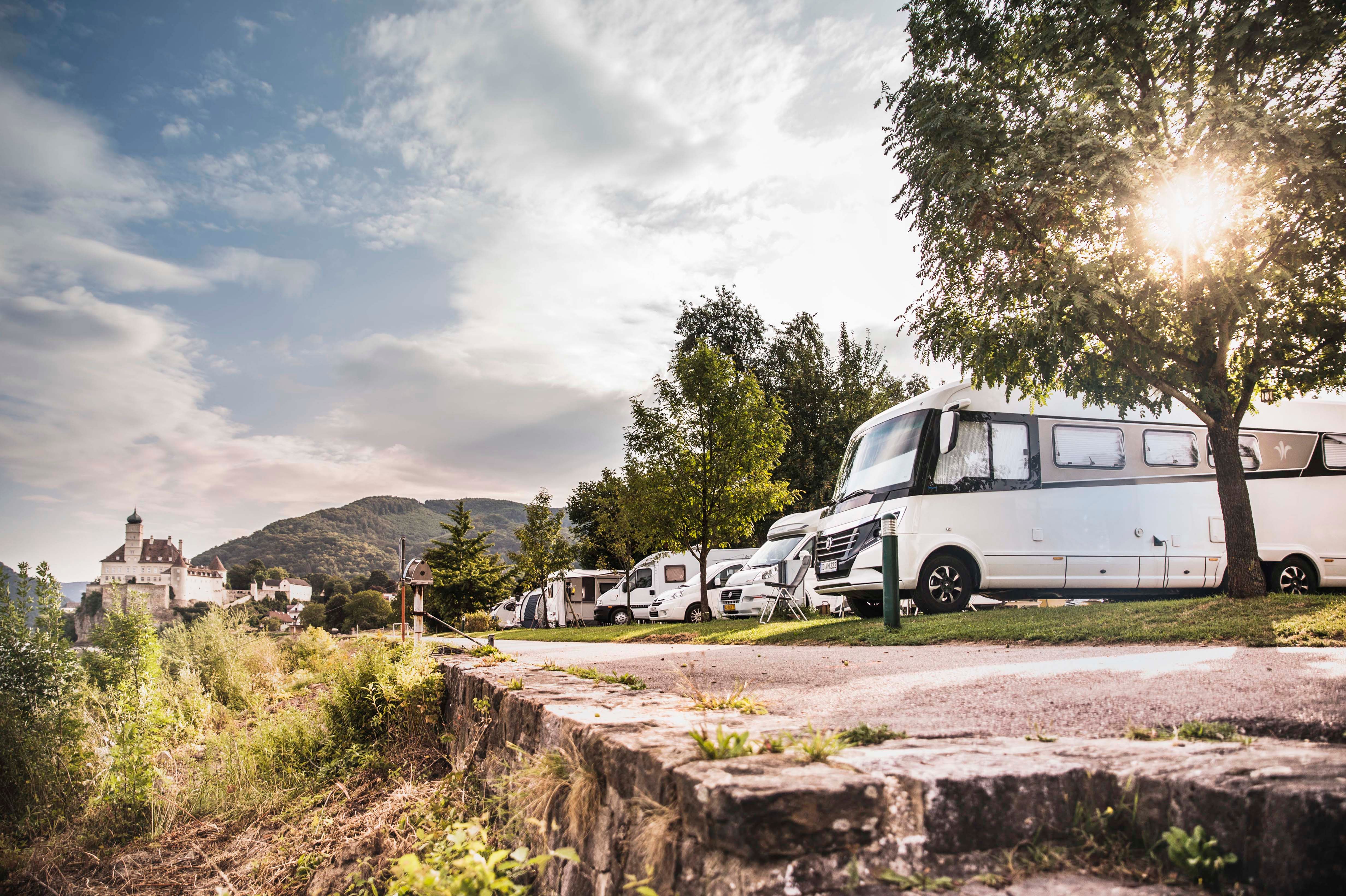 Wohnmobile auf einem Campingplatz mit Schloss Schönbühel im Hintergrund.
