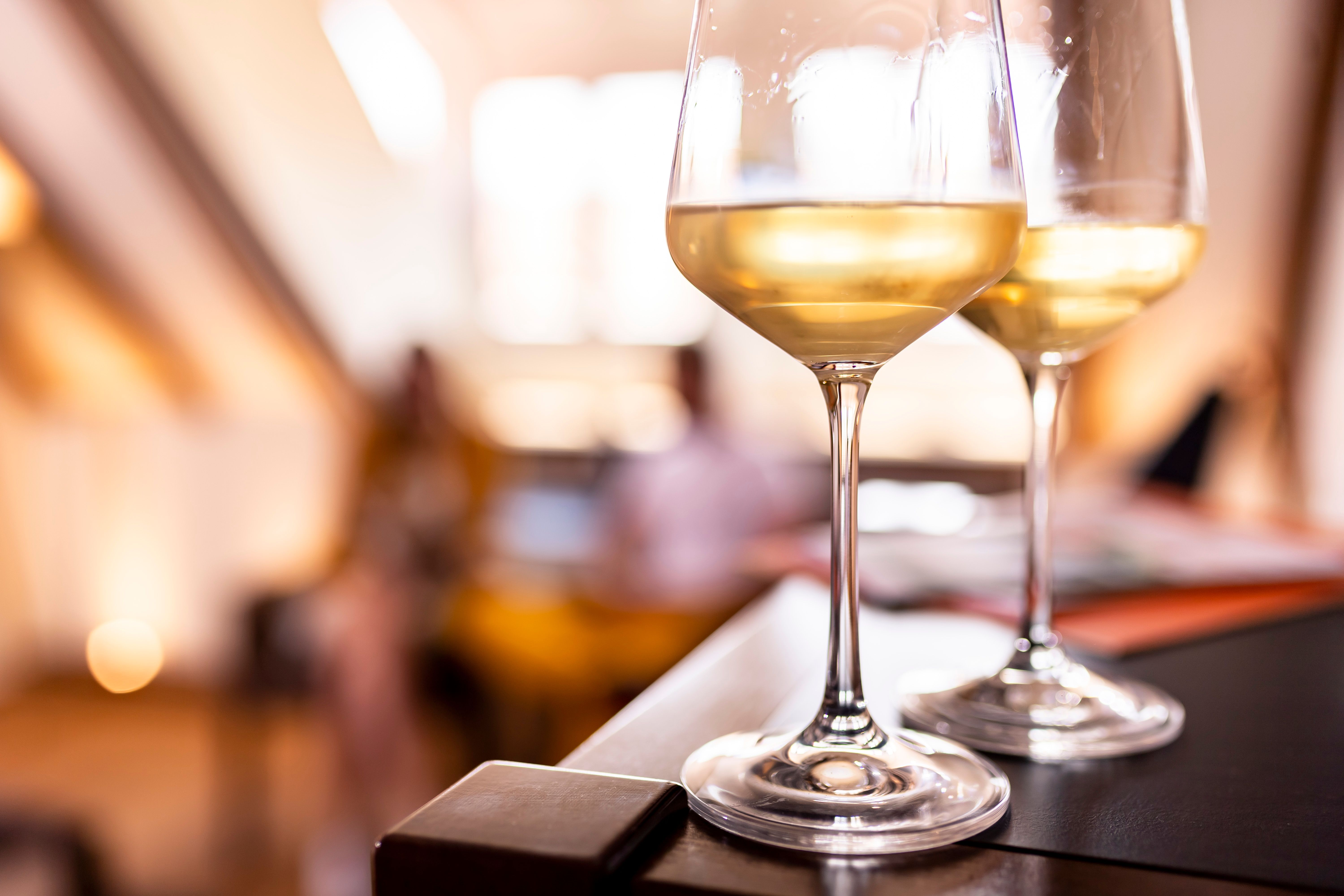 Zwei Gläser Weißwein auf einem Tisch, unscharfer Hintergrund mit warmem Licht.