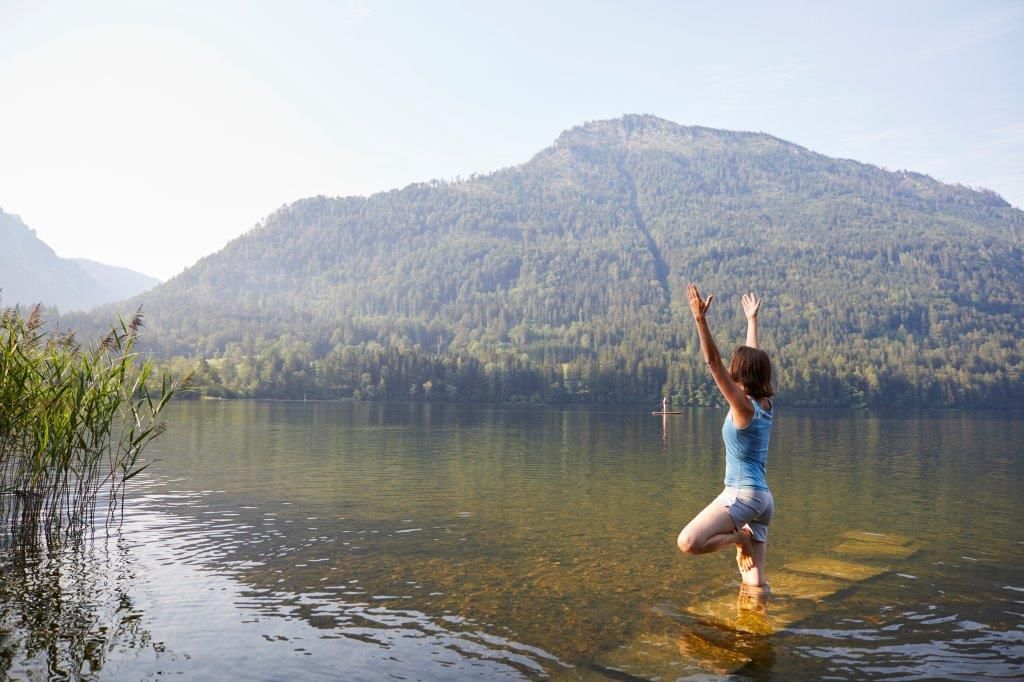 Eine Frau macht Yoga in einem See mit einem Berg im Hintergrund.