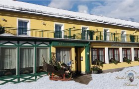 Gelbes Geb&auml;ude mit gr&uuml;nen Akzenten, beschriftet als Gasthof Schmirl, im Schnee.