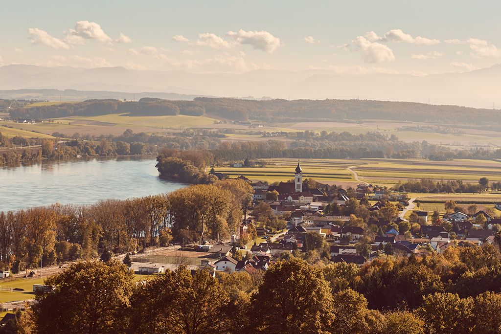 Landschaftsansicht von Gottsdorf im Nibelungengau mit Fluss und Kirche.